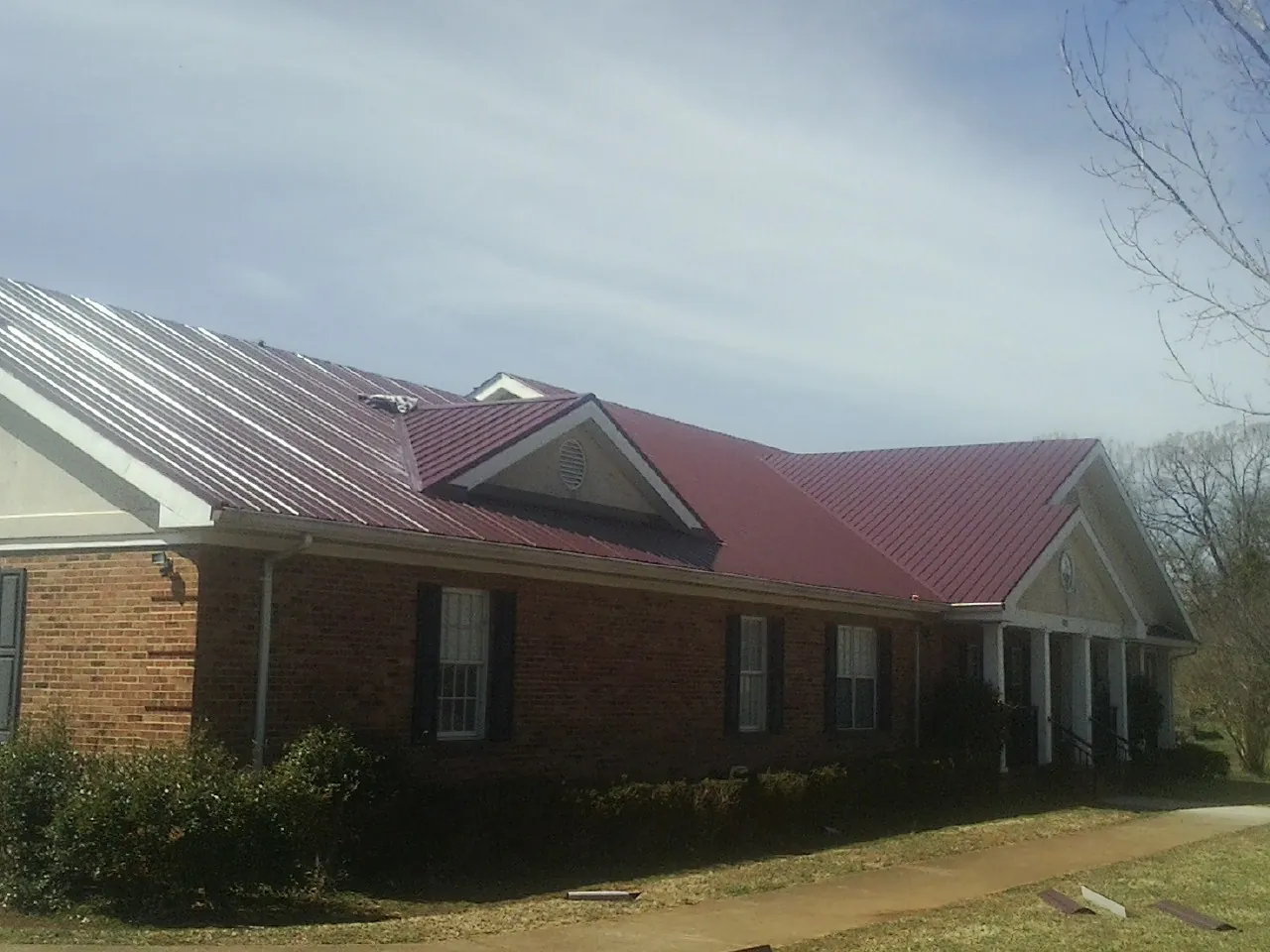 Red metal roof with gabled entries on a long brick building, from a Hail Damage Roof Repair job in Stonewall