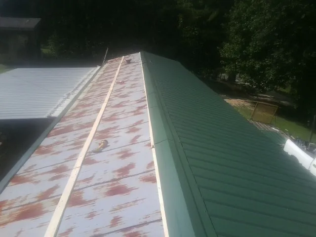 Old rusted panels beside newly installed green metal roofing — Wind Damage Roof Repair by Roofing Brothers in Stonewall