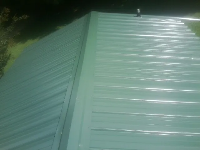 New green metal panels meeting at the ridge of a roof — Flat Roof Repair work by our crew in Stonewall