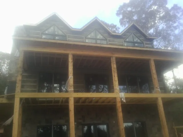 Dormers and porch framing on a large log home under construction — Roof Coating work by our crew in Stonewall