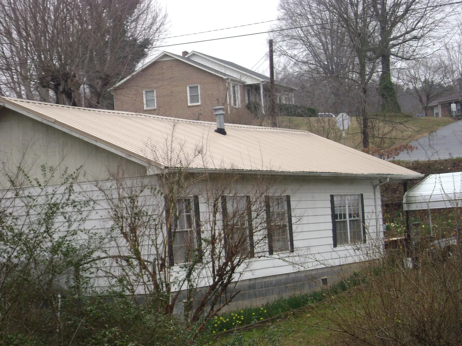 Tan metal roof on a white sided house set into a hillside — Commercial Roofing by Roofing Brothers in Stonewall