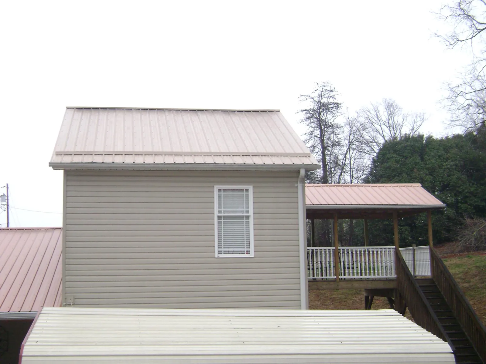 Tan metal roofs on a two story addition and attached porch, from a Roof Replacement job in Stonewall