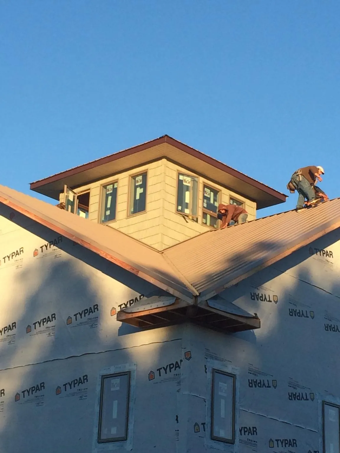 Roofers working around a rooftop cupola on a new metal roof at sunset — Roof Waterproofing in Stonewall by Roofing Brothers